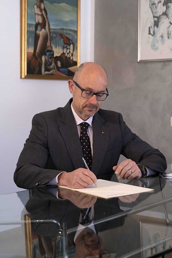 Matteo della Pietra seduto alla scrivania nel suo studio, impegnato in attività legali e consulenze, rappresentando la professionalità della famiglia della Pietra.