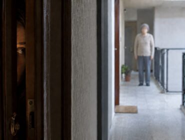 Giovane donna guarda con timore dalla porta socchiusa una persona sul pianerottolo che la aspetta o la controlla